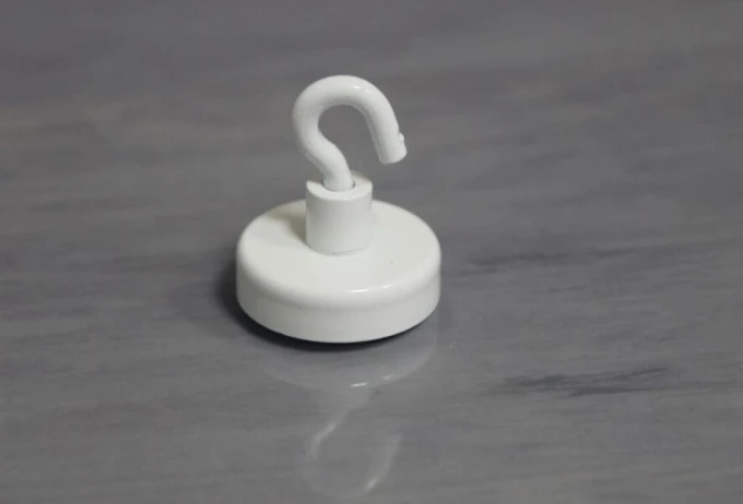 Round magnet with a white hook on a smooth surface, available in various sizes and graphic designs.