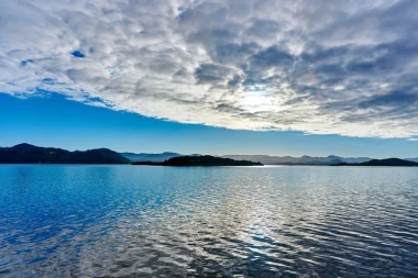 Wall mural of small islands seen from afar FP 1414 - Graphic design. Water reflects the sky, with islands and mountains in the background.