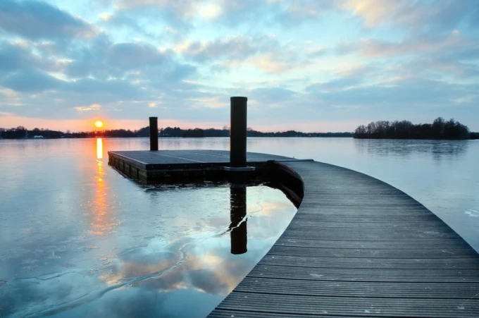 Wall mural of a pier at sunset, featuring a graphic design with water reflections of the sun and clouds.