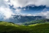 Wall mural featuring a stunning view of green meadows, mountains in the background, and clouds in the sky.