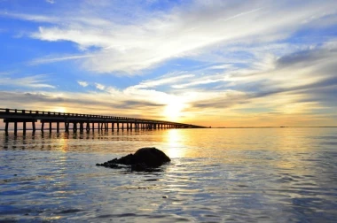 Sunset wall mural with pier view FP 2022 - Graphic design featuring pier, water, and clouds in various shades.