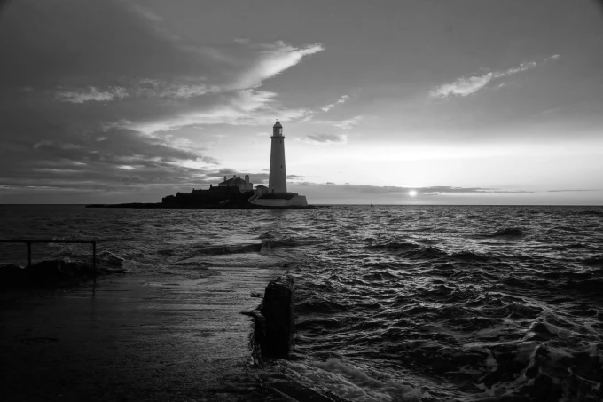Wall mural of the last rays of sun over a lighthouse, graphic design with a lighthouse against waves.