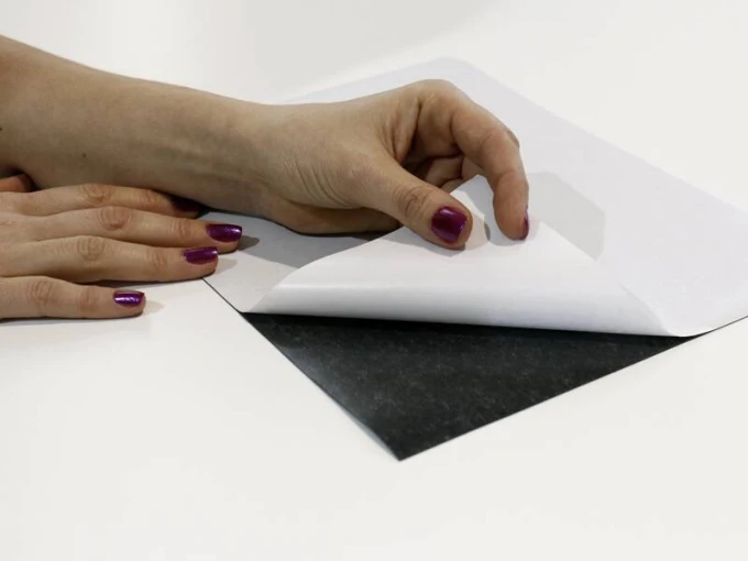 Self-adhesive steel foil A4 sheet - Graphic design. Black background with white paper, hand peeling off the foil.