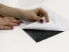 Self-adhesive steel foil A4 sheet - Graphic design. Black background with white paper, hand peeling off the foil.