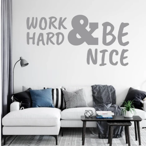 Wall sticker with the phrase "Work hard and be nice" - Living room decor. Light-colored walls, sofa with cushions.