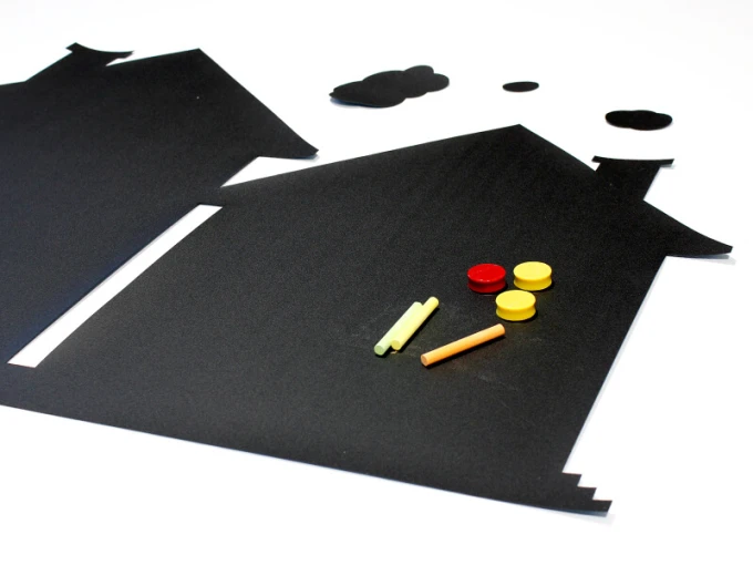 Chalkboard magnetic house 261 - Black house-shaped board with colorful magnets and chalks.