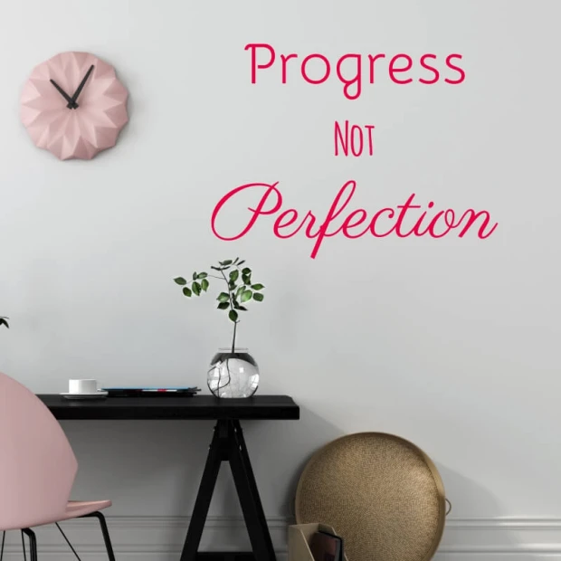 Wall sticker Progress not perfection 2513 - Living room decor. Light-colored walls, table, and clock in pastel shades.