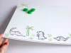 Dry-erase magnetic board for kids featuring dinosaur and palm graphics on a white background.