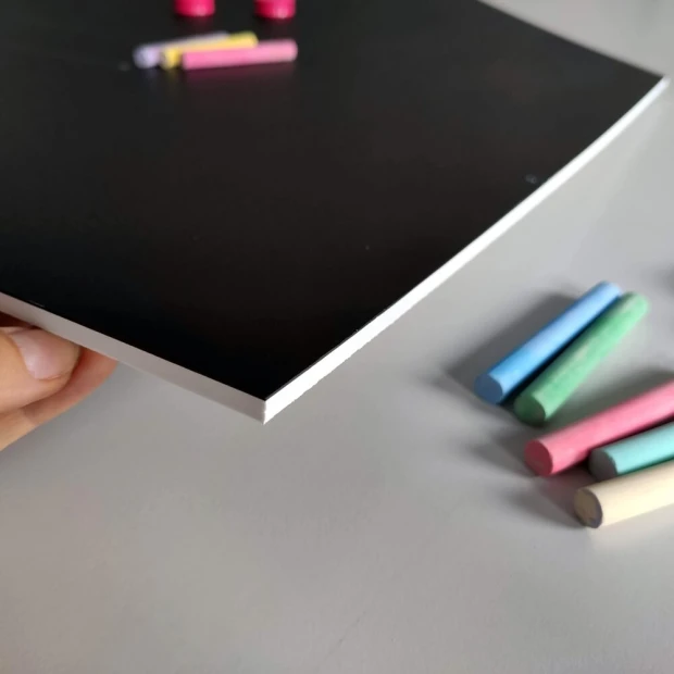 Chalkboard magnetic board for kids, house design. Simple black surface with colorful chalks beside it.