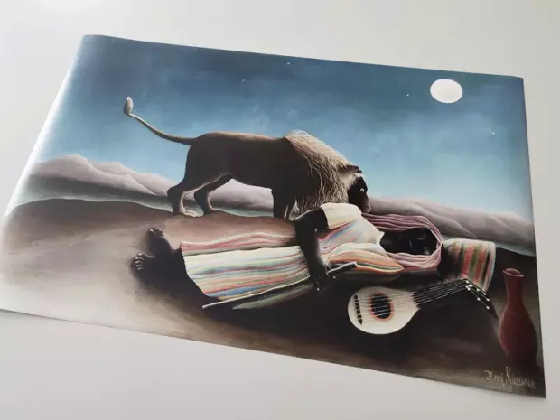 Reproduction of La zingara addormentata by Henri Rousseau. A figure lies on the ground with a lion nearby and mountains in the background.