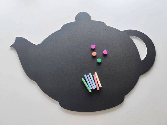 Chalkboard magnetic board for kitchen in teapot shape with colorful magnets and chalks.