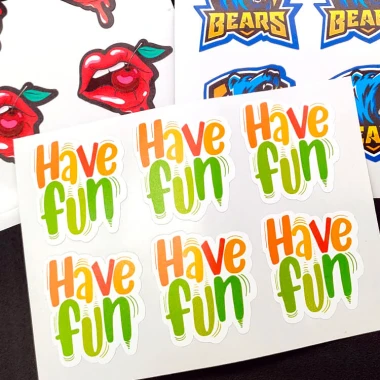 Custom-shaped adhesive labels on a sheet - graphic design. Shapes include lips, text, and logos in various colors.