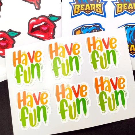 Custom-shaped adhesive labels on a sheet - graphic design. Shapes include lips, text, and logos in various colors.