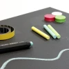 Chalkboard magnetic foil with colorful chalks and round magnets on a black background.