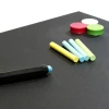 Chalkboard magnetic foil with colorful chalks and round magnets on a black background.