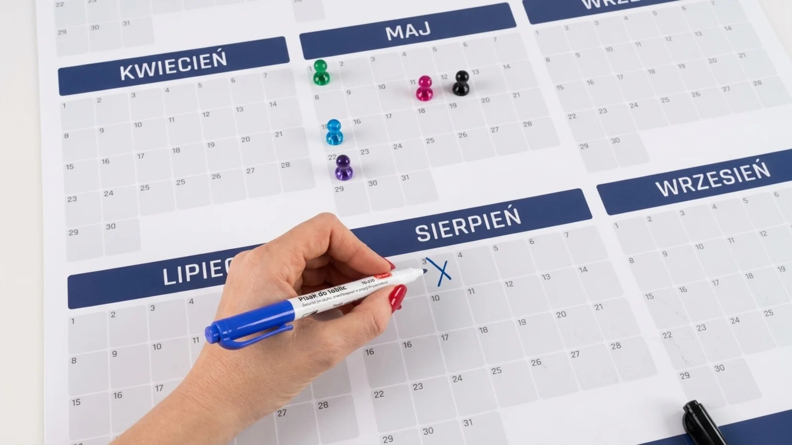 A hand marking an annual dry wipe planner with a pen